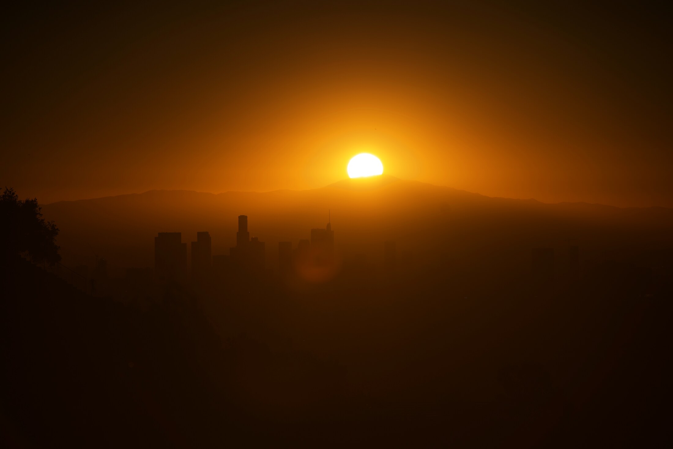 The sun dropping behind the hills over downtown Los Angeles, sky a haze of orange