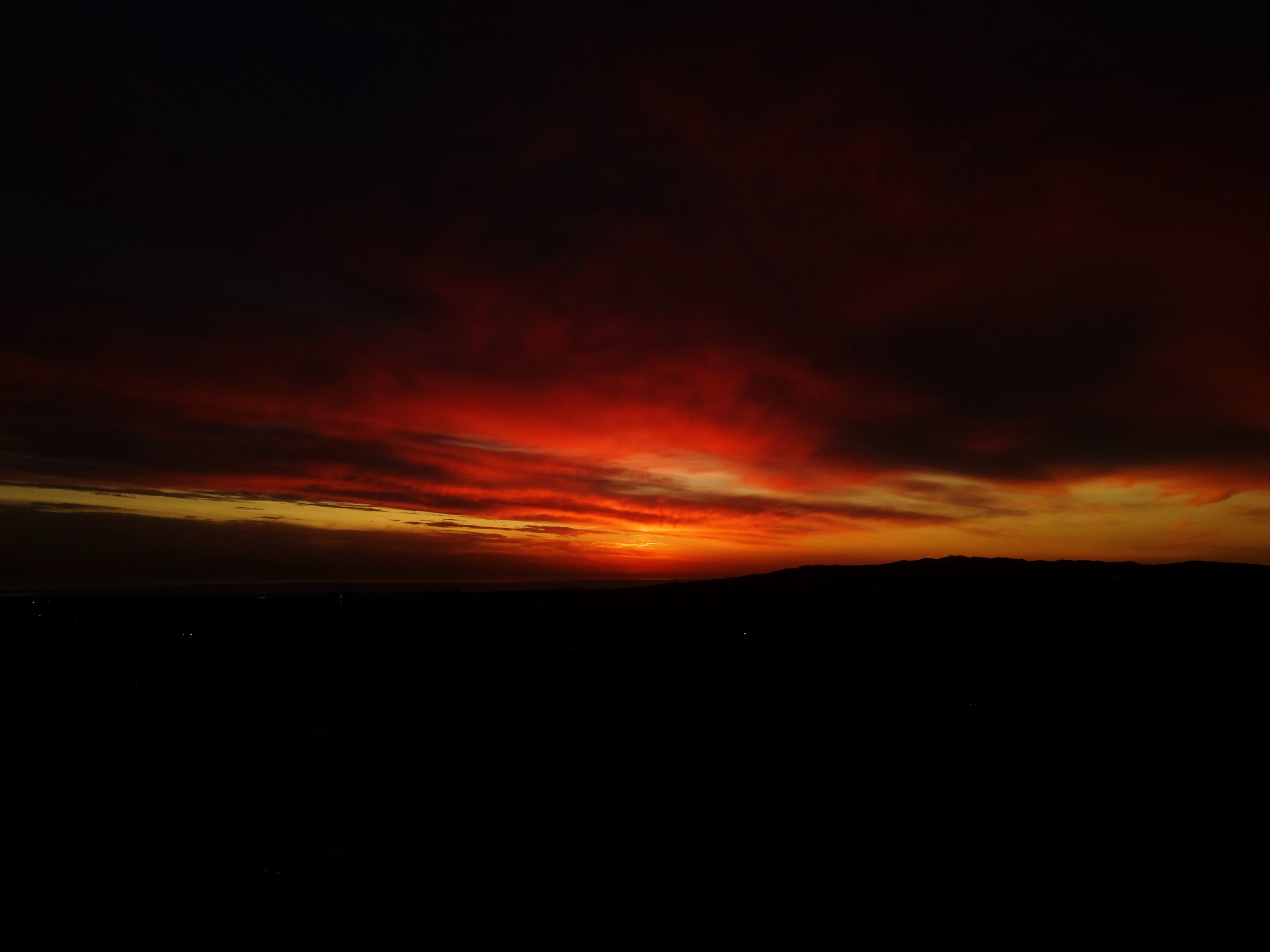 Blood-red sunset clouds burning out over a black horizon line