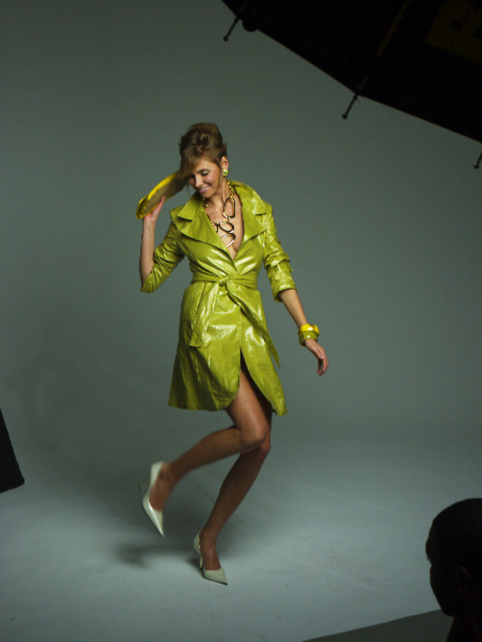Model mid-step in a glossy chartreuse trench coat on a gray studio cyclorama