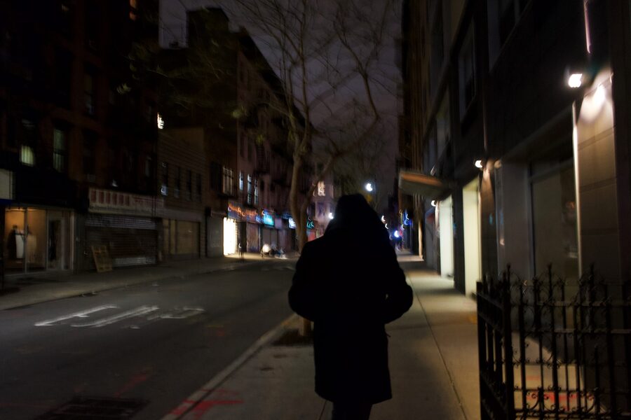 Hooded figure from behind walking down a dark, empty downtown street