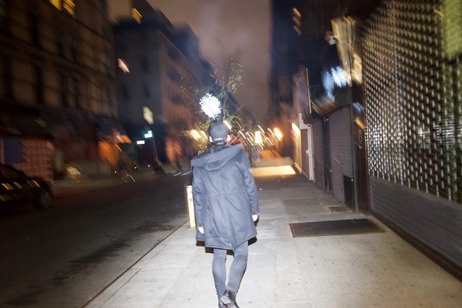 Figure walking away down an empty sidewalk at night, coat burned white by the flash like a ghost