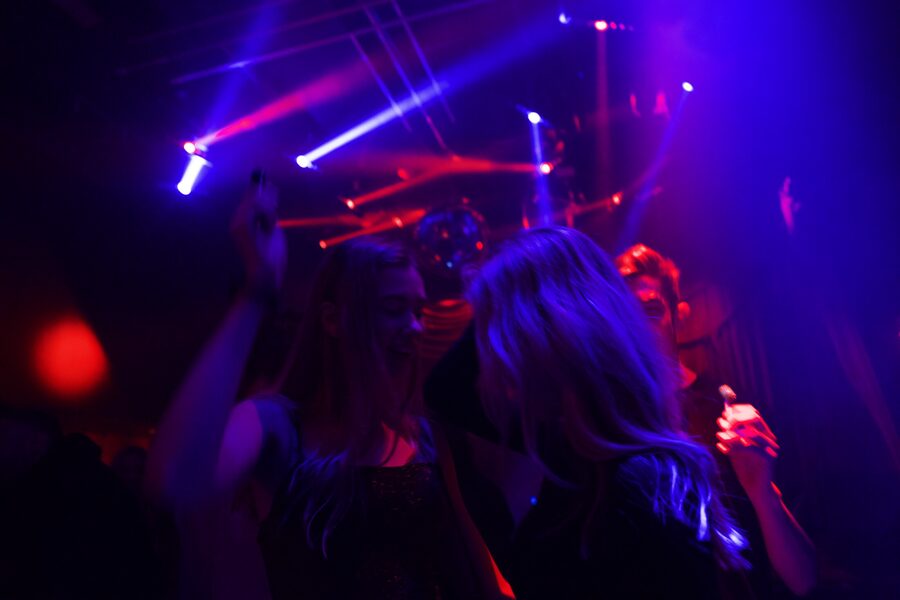 Two women dancing under purple lasers and a disco ball, hair catching the beams