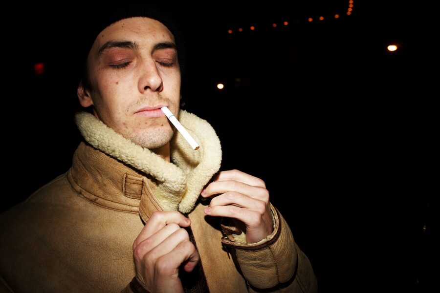 Man in a shearling collar lighting a cigarette in the dark, flash freezing the match-strike