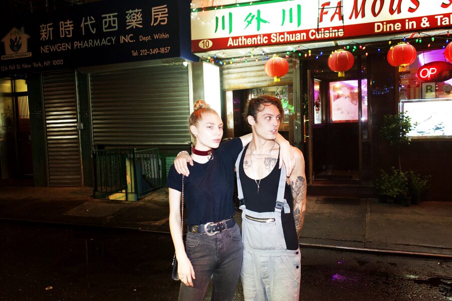 Tattooed couple in suspenders and black standing on a wet Chinatown street under red lanterns and neon restaurant signs