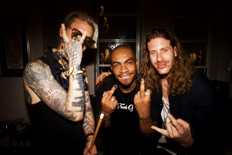 Three grinning friends at a party flipping middle fingers at the flash, tattooed arms front and center